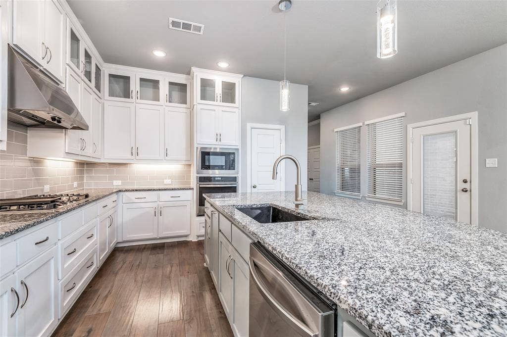 636 Courtyard Lane, Irving, TX 75039 Kitchen featuring white shaker cabinetry, stainless steel appliances, granite countertops, wood-finish flooring, and a subway tile backsplash