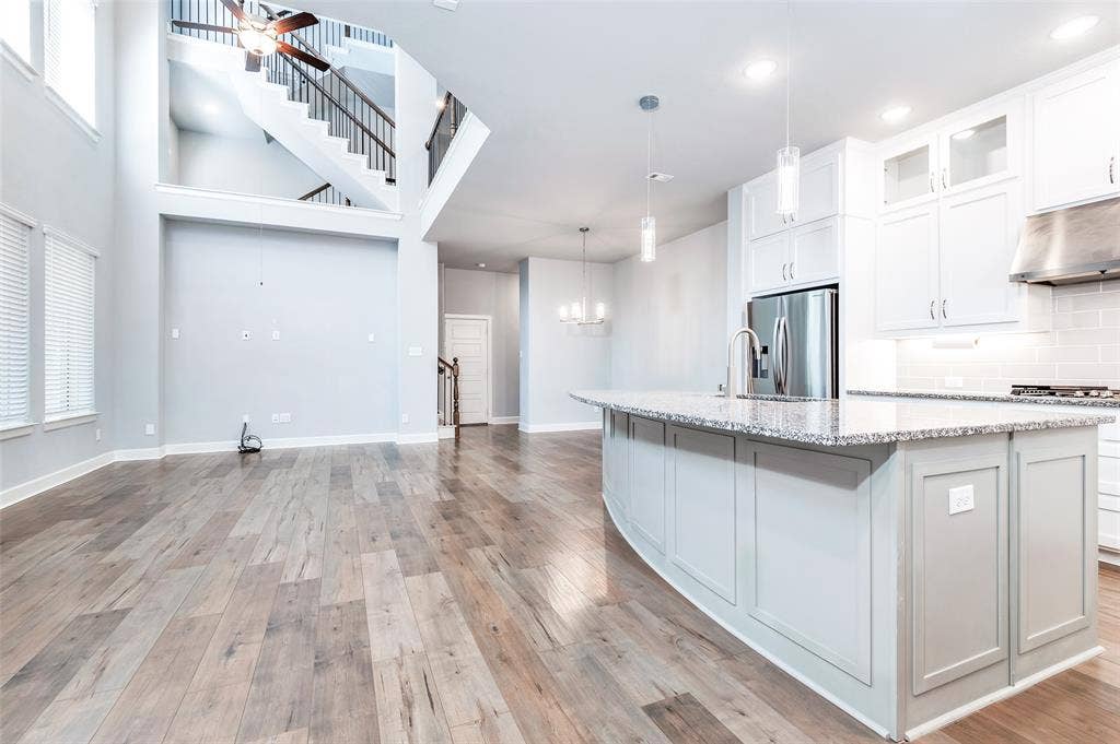 636 Courtyard Lane, Irving, TX 75039 Open-concept living area featuring wood-finish flooring, a two-story ceiling, and a modern kitchen with a large island and stainless steel appliances