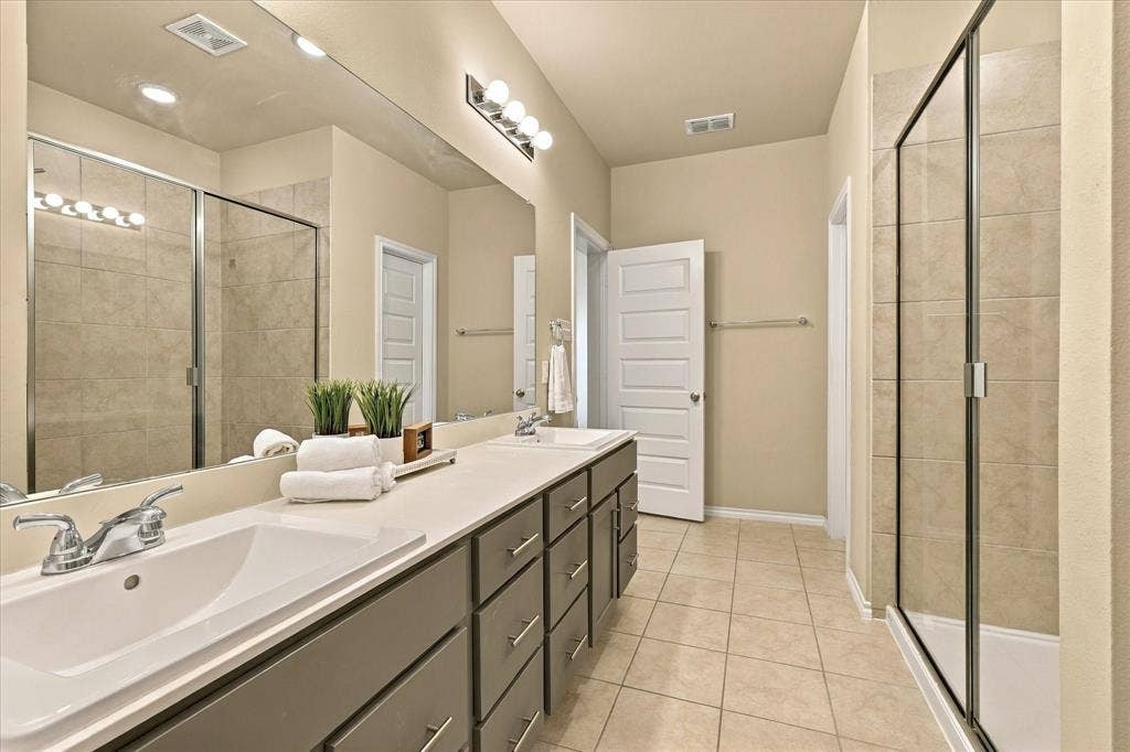 6304 Jib Court, Fort Worth, TX 76179 Dual vanity with integrated sinks, extensive countertop space, multiple storage drawers, a large wall-mounted mirror, and a glass-enclosed shower