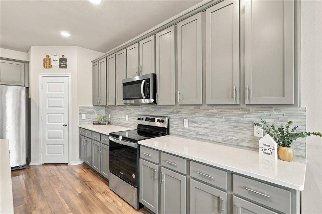 6304 Jib Court, Fort Worth, TX 76179 Wood-finish flooring, light gray cabinetry, stainless steel appliances, white countertops, and a full-height tile backsplash