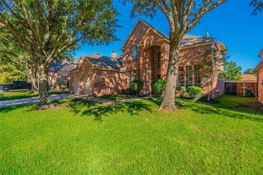 Brick exterior, arched entryway, two-car garage, mature trees, and a well-maintained lawn