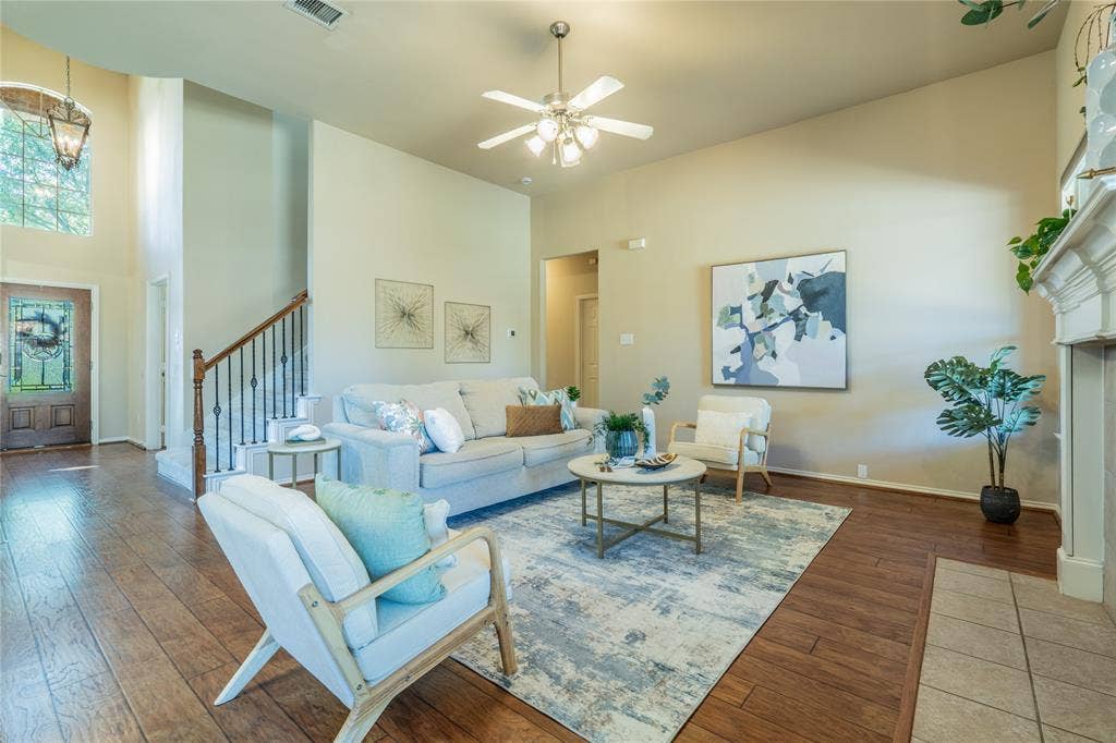 Spacious living area featuring wood-finish flooring, a ceiling fan, and a fireplace with a white mantel