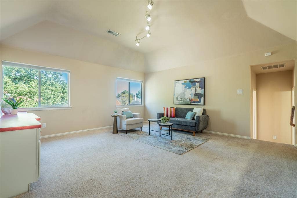 Upstairs game room with a vaulted ceiling with track lighting, multiple windows, and neutral carpeting