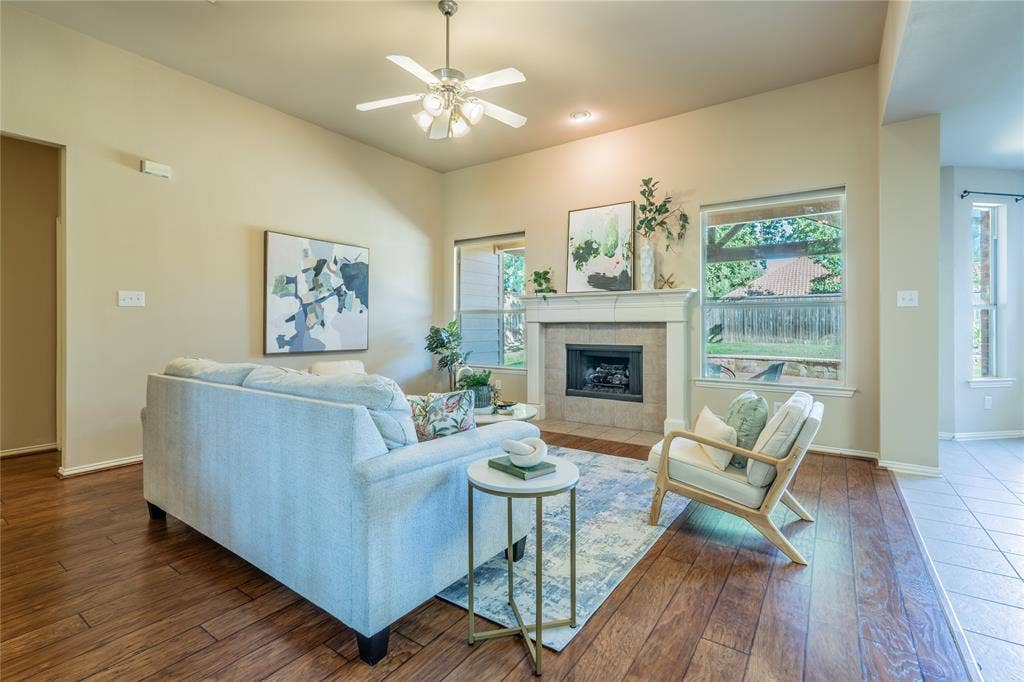 Spacious living area featuring wood-finish flooring, a tiled fireplace with a mantel, and multiple windows