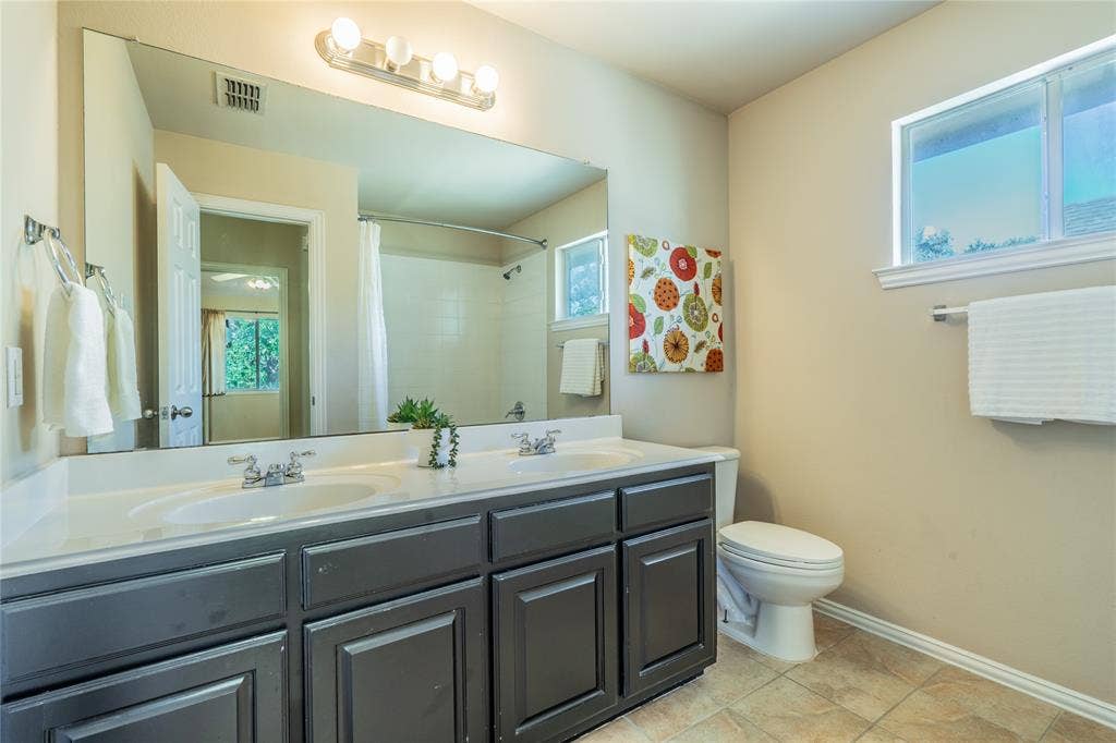 Bathroom with double vanity with integrated sinks, large wall-mounted mirror, ceramic tile flooring, and a window for natural light