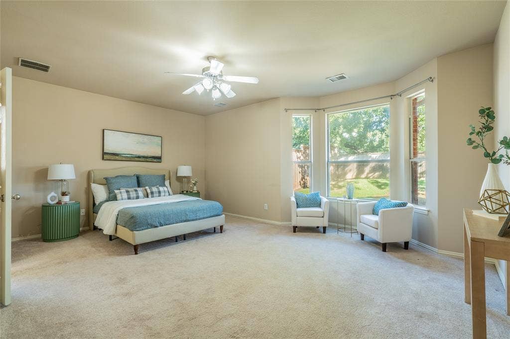 Expansive primary bedroom featuring carpeted flooring, a ceiling fan, and a prominent bay window