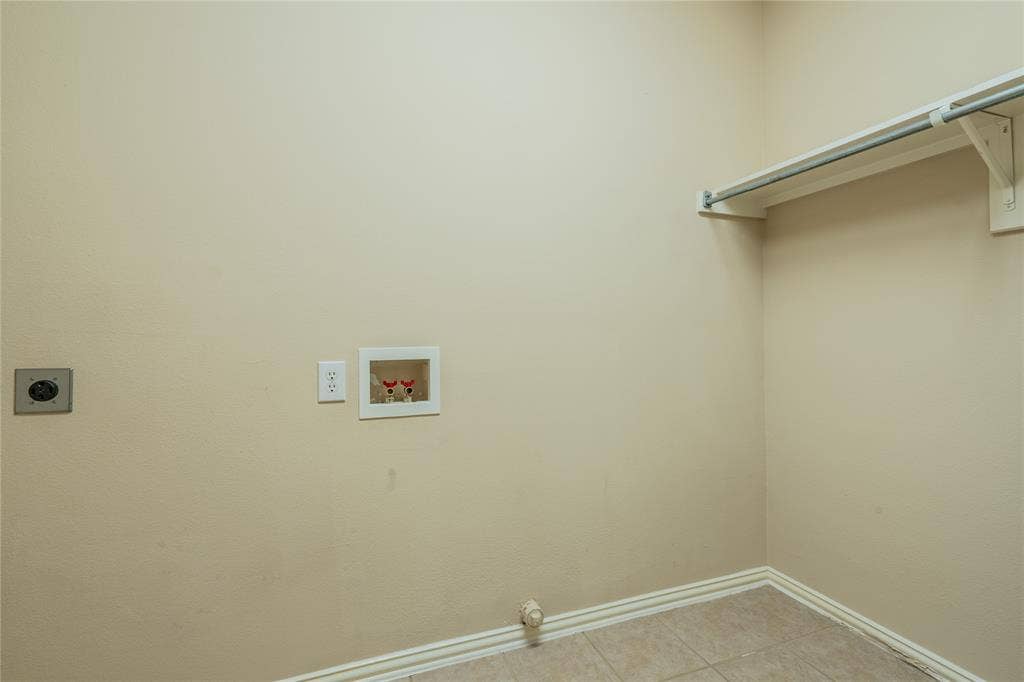 Laundry area with tiled flooring, neutral wall paint, overhead shelving, and integrated utility connections