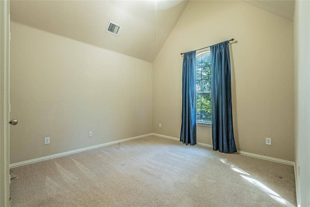 Bedroom with a vaulted ceiling, neutral wall paint, carpeted flooring, single window, and a door with a satin nickel doorknob