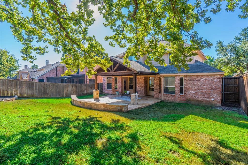 Manicured backyard featuring a covered patio, extensive hardscaping, and privacy fencing