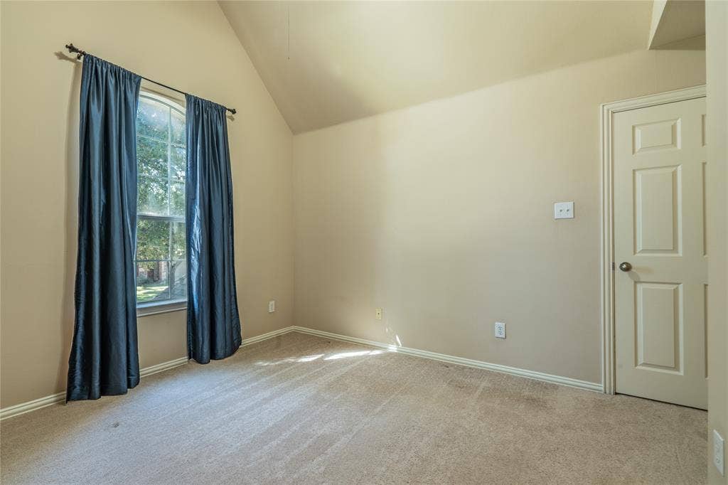 Another view of the bedroom with a vaulted ceiling, carpeted flooring, and a paneled interior door