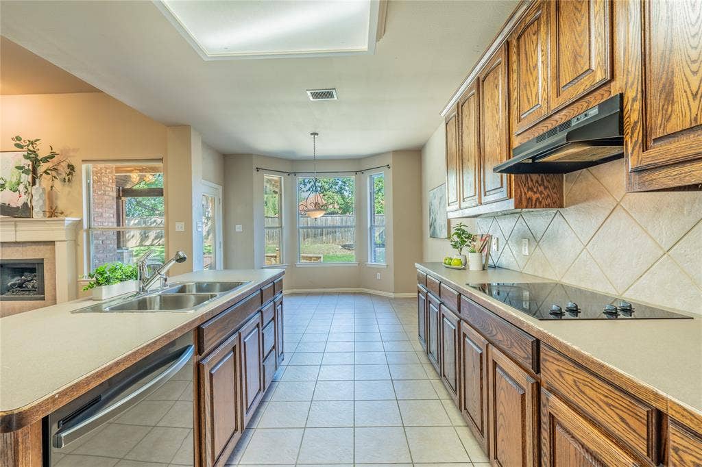 Kitchen featuring tile flooring, wooden cabinetry, an electric cooktop, a double basin sink, and a tiled backsplash