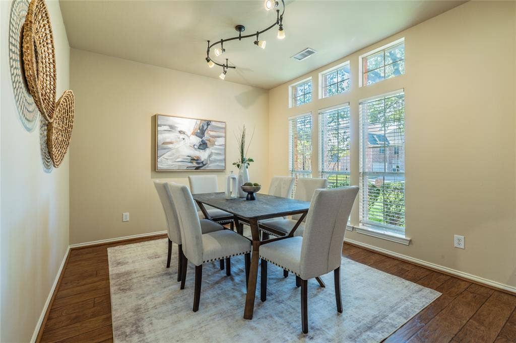 Vaulted ceiling with track lighting, multiple large windows, wood-finish flooring, and neutral wall tones