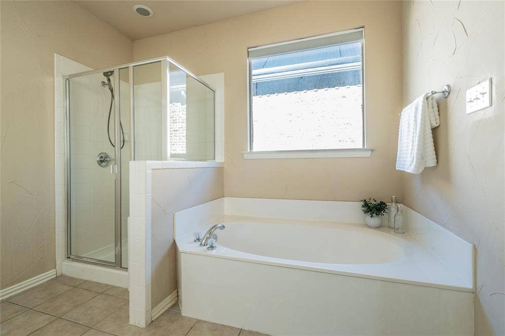 Primary bathoorm with corner soaking tub, glass-enclosed shower, and a large window