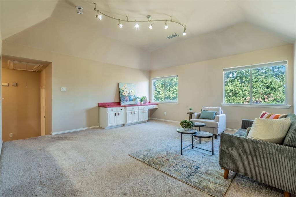 Upstairs game room with vaulted ceiling with track lighting, dual windows, built-in lower cabinetry with a red countertop, and carpet flooring
