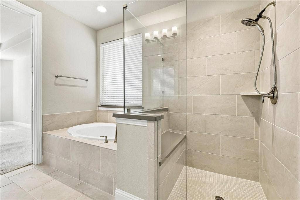 Spacious bathroom featuring a built-in soaking tub, a tiled walk-in shower with bench seating, and a dual-head shower system