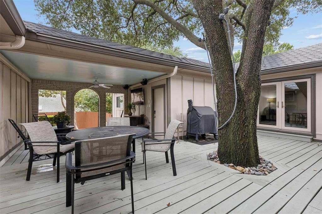 Courtyard Living Under the Trees — The spacious deck wraps around mature trees and connects multiple interior spaces, creating a shaded outdoor setting for dining, relaxing, and entertaining.