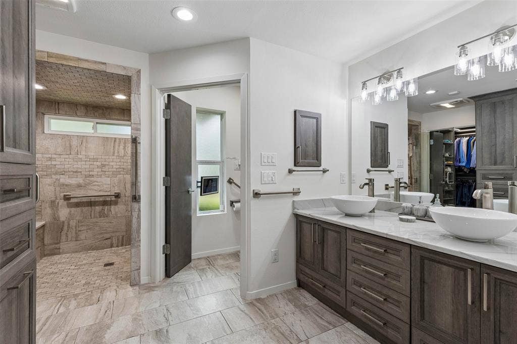 Remodeled Primary Bath with Thoughtful Storage — Dual vessel sinks, extensive cabinetry, updated lighting, and a spacious layout create a highly functional bath designed for everyday comfort.