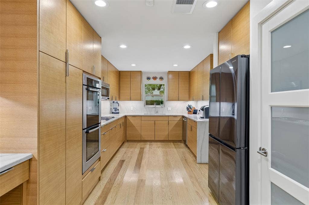 Remodeled Kitchen with Clean Modern Lines — Warm-toned cabinetry, extensive counter space, hardwood flooring, and a streamlined layout give this kitchen a polished, highly functional feel.
