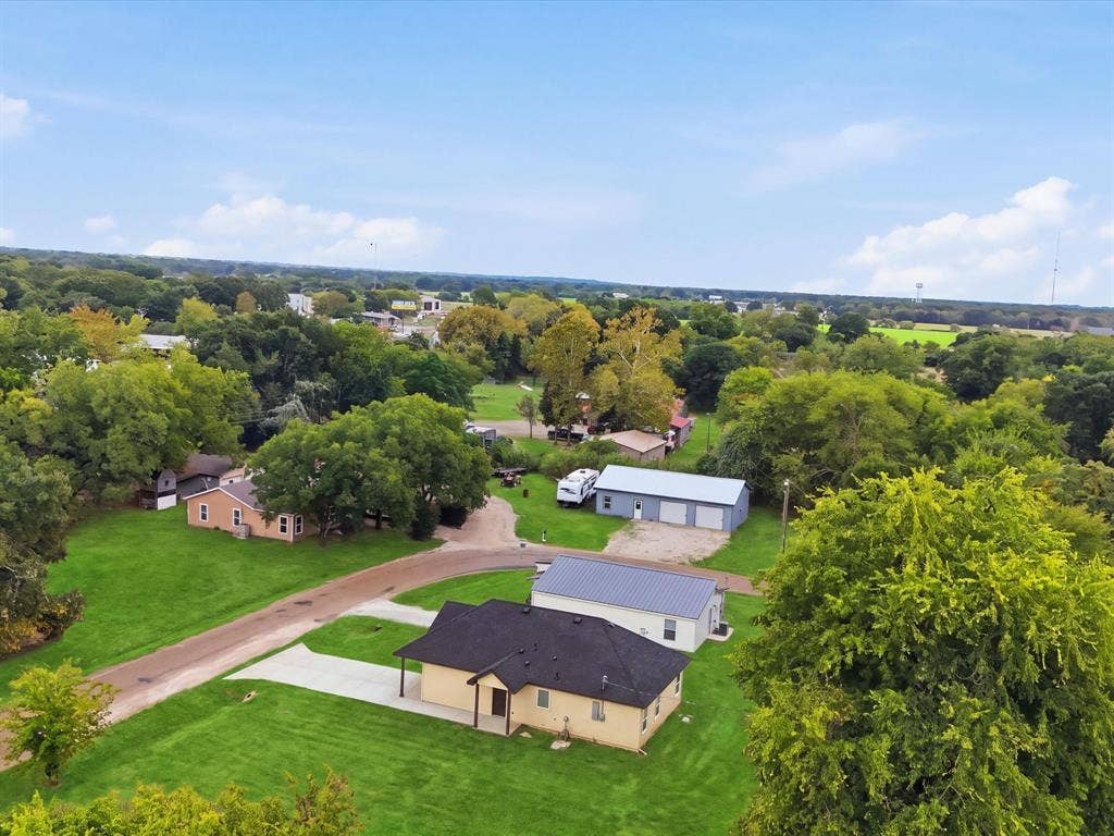 105 Oak Ridge Road, Mabank, TX 75156 Expansive property with a single-story residence featuring a dark shingle roof and a cream-colored exterior, accompanied by a separate multi-bay garage structure