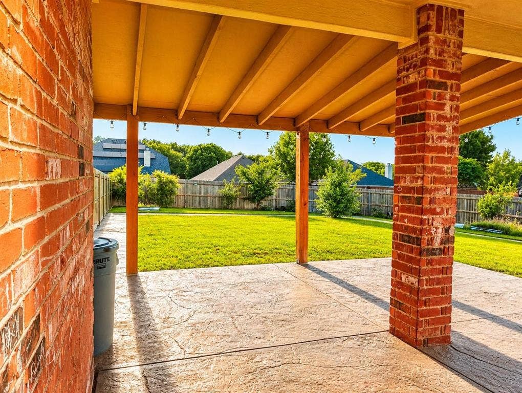 1114 Hidden Creek Drive, Allen, TX 75002 Covered patio featuring a stamped concrete surface, brick support columns, and a level lawn beyond