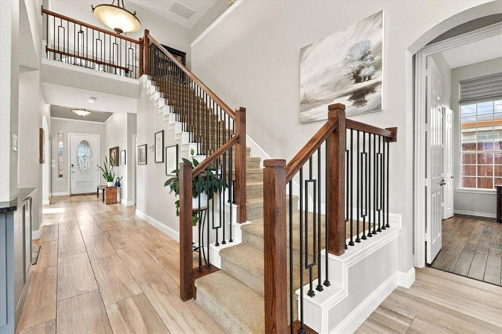 Foyer featuring wood-finish flooring, a staircase with a stained wood handrail, and decorative matte black iron balusters