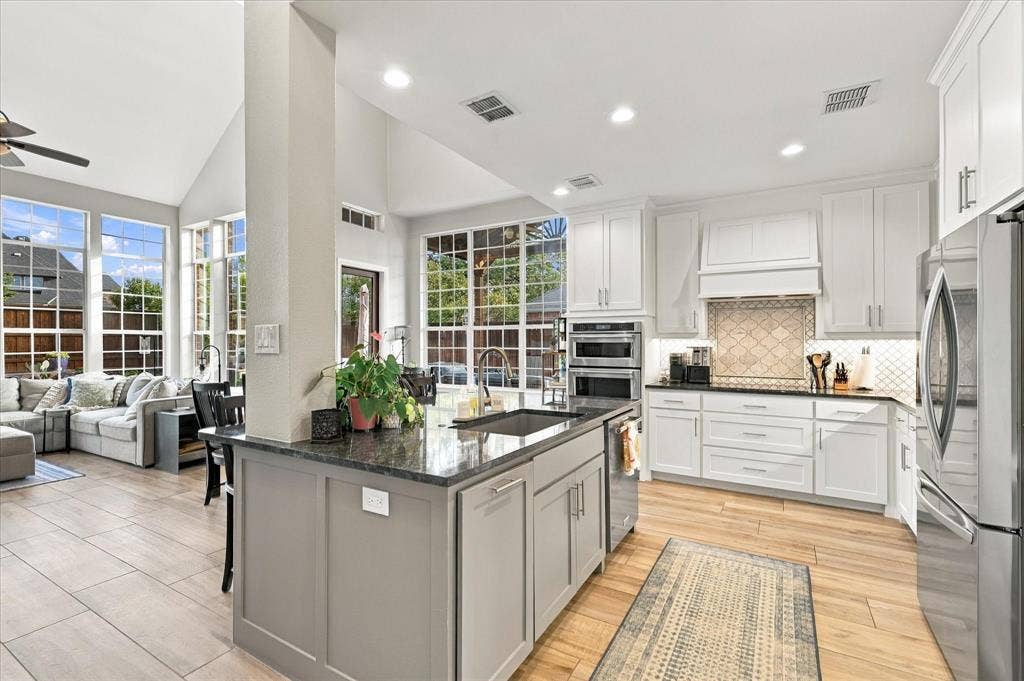 Kitchen featuring white cabinetry, stone-finish countertops, stainless steel double wall ovens, a large center island with an undermount sink, and wood-finish tile flooring