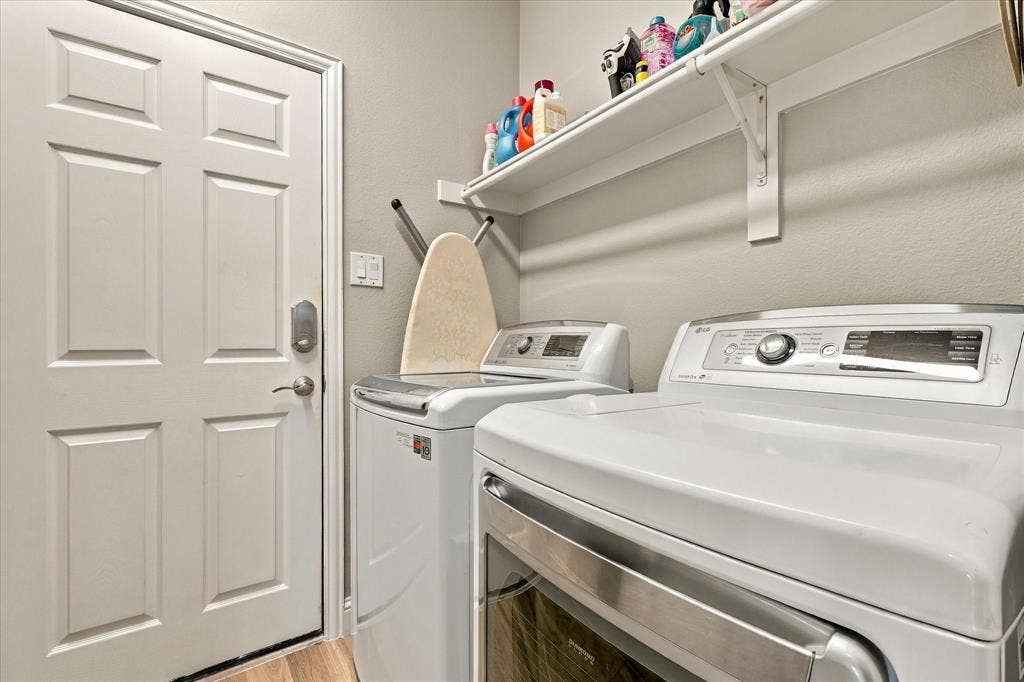 Laundry area featuring a white six-panel door, built-in upper shelving, and wood-finish flooring
