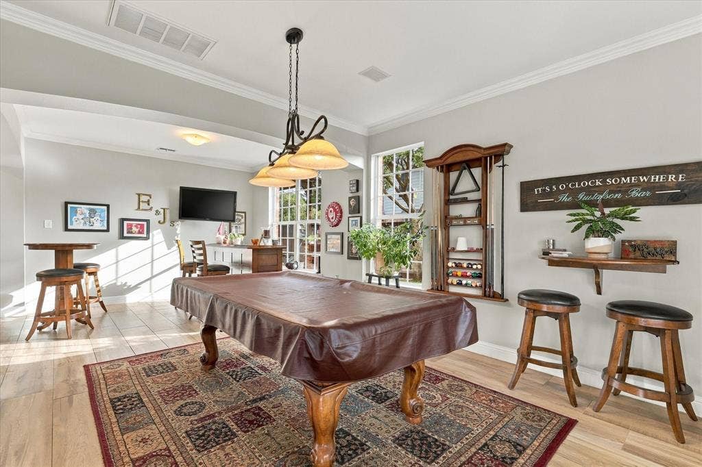 Open-concept area featuring wood-finish flooring, multi-light chandelier with glass shades, tall multi-pane windows, and crown molding