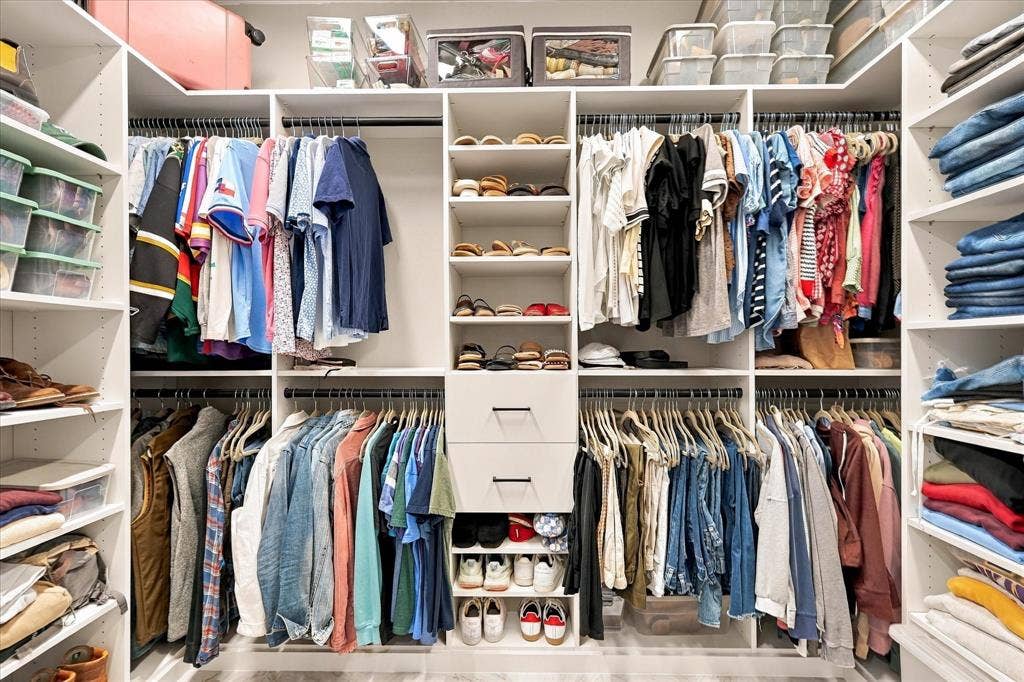 Custom walk-in closet featuring white built-in shelving, dual hanging rods, a central column of open storage cubbies, and two integrated drawers with matte black hardware