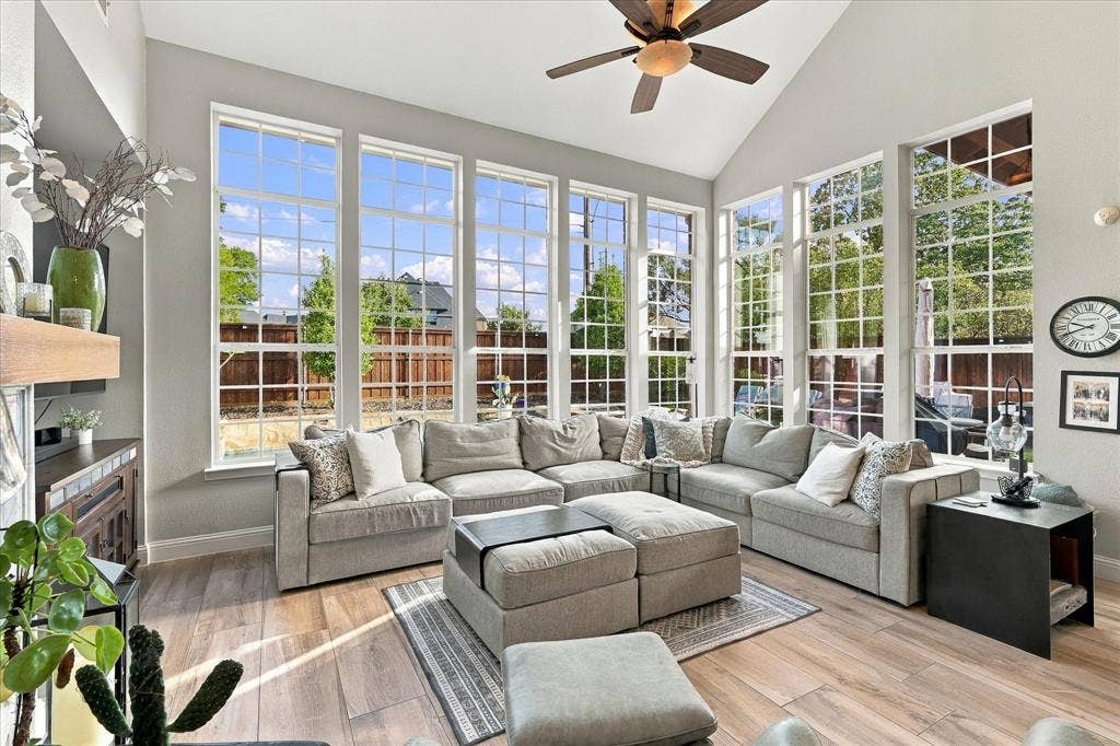 Living area featuring a vaulted ceiling, floor-to-ceiling windows with grid detailing, wood-finish tile flooring, and a ceiling fan
