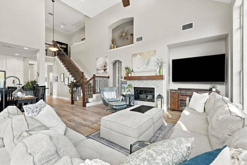 Vaulted ceilings featuring an open staircase with decorative iron balusters, a fireplace with a wood mantel and tile surround, and wood-finish flooring