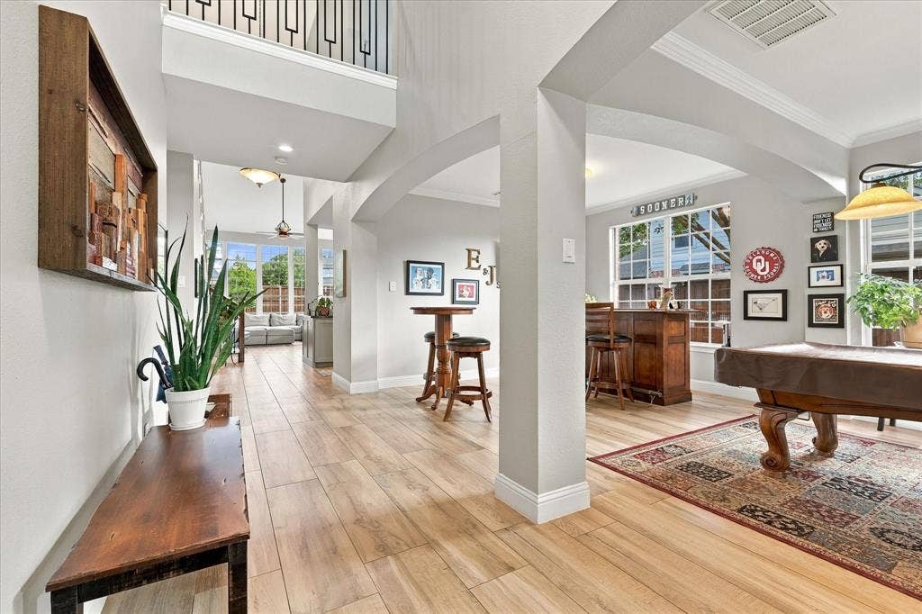 Open-concept interior featuring wood-finish flooring, high ceilings, architectural arched doorways, and metal-railing stair detail