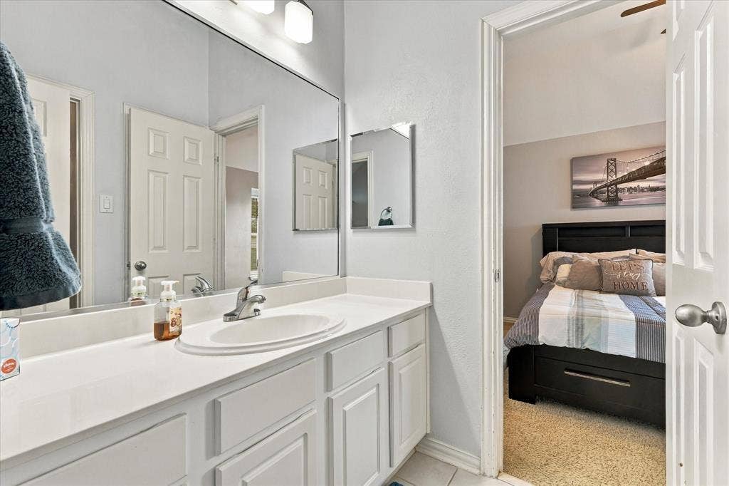Vanity with a solid-surface countertop, an integrated oval sink, chrome faucet, wall-spanning mirror, and white shaker-style cabinetry