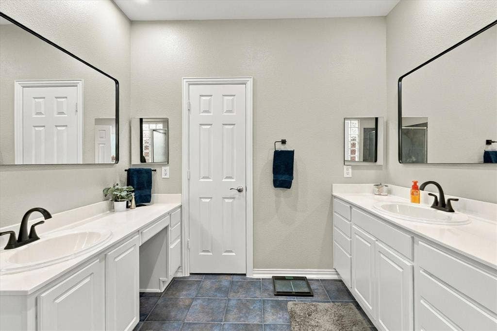Dual vanity featuring white cabinetry, solid-surface countertops, integrated porcelain sinks, matte black fixtures, and expansive wall-mounted mirrors