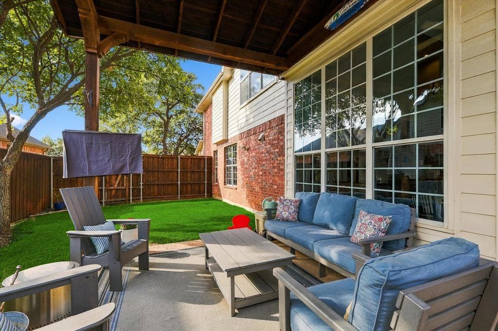 Covered patio featuring a concrete floor and wood-paneled ceiling, exterior brick and siding, multi-pane windows, and a fenced backyard with artificial turf
