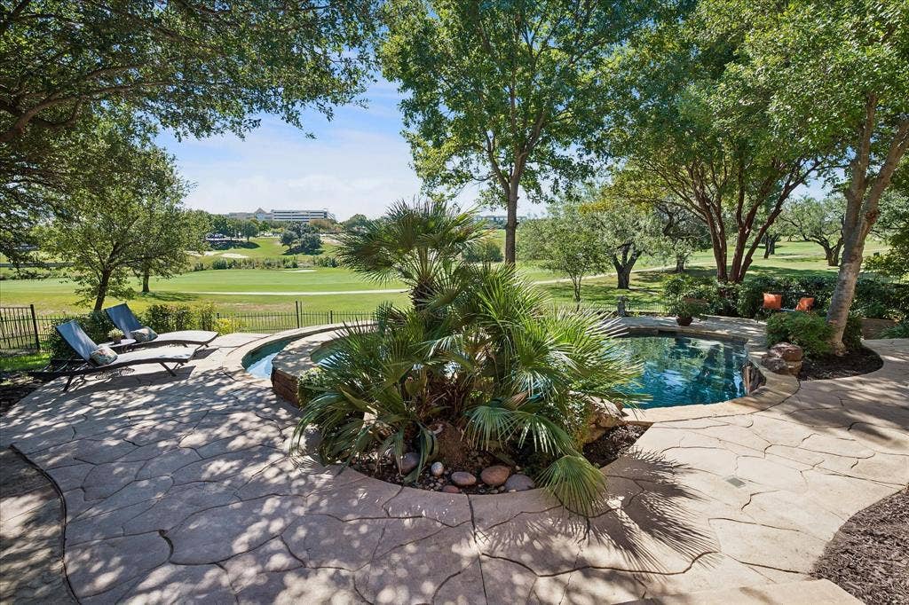 2204 Creekside Circle S, Irving, TX 75063 Terraced flagstone patio with a built-in swimming pool and integrated spa, surrounded by mature trees and lush landscaping