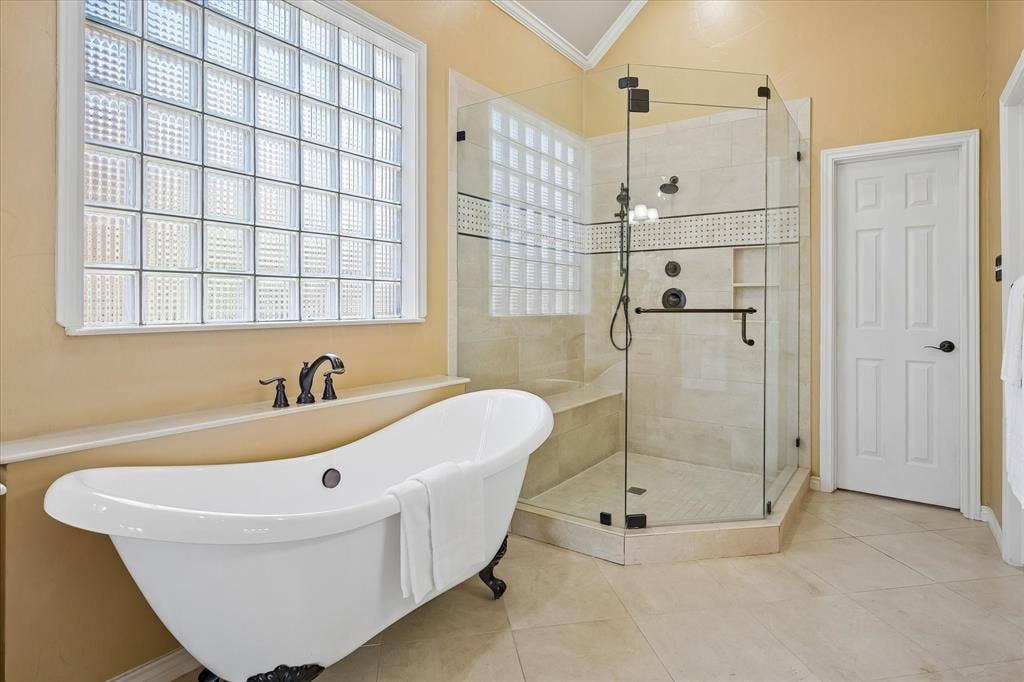 2204 Creekside Circle S, Irving, TX 75063 Freestanding soaking tub with bronze fixtures and feet, glass block window, and a frameless glass-enclosed shower with a built-in bench. Two large walk in closets for plenty of storage!
