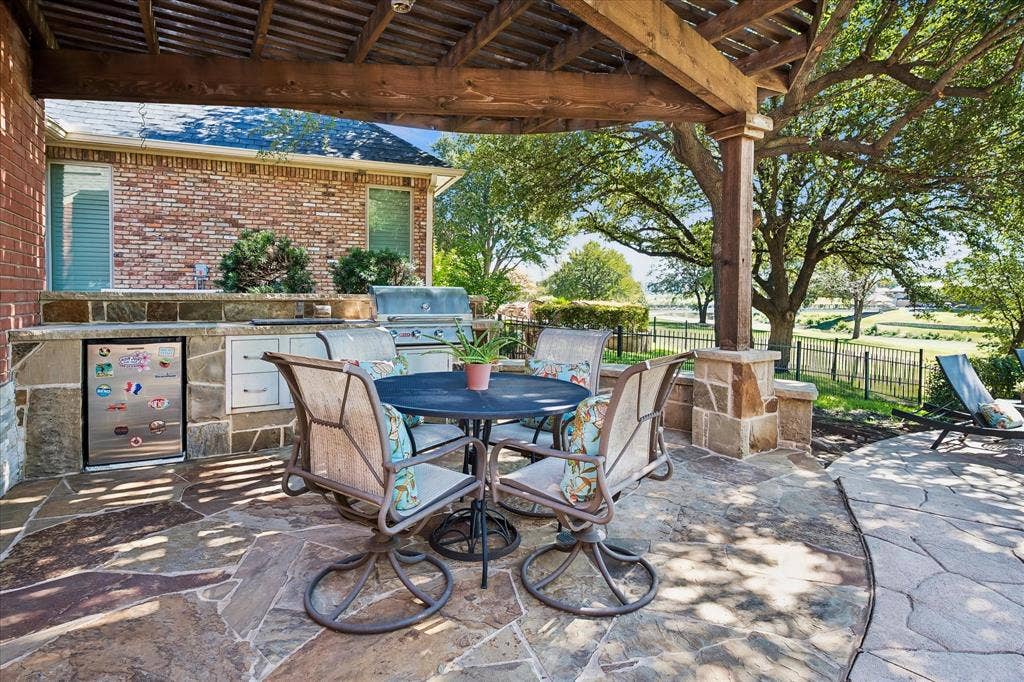 2204 Creekside Circle S, Irving, TX 75063 Outdoor patio featuring flagstone flooring, a built-in outdoor kitchen with a grill, refrigerator, storage drawers, and a wood pergola