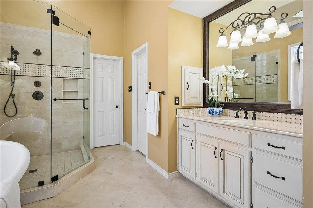 2204 Creekside Circle S, Irving, TX 75063 White vanity with bronze hardware, framed mirror, glass-enclosed shower with porcelain tile surround, built-in shower niche, and porcelain tile flooring.