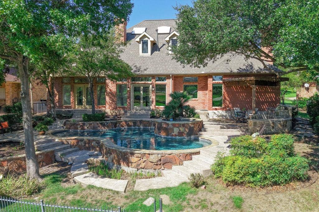 2204 Creekside Circle S, Irving, TX 75063 Brick exterior with multiple windows, tiered swimming pool with integrated spa, stone retaining walls, and a stone patio