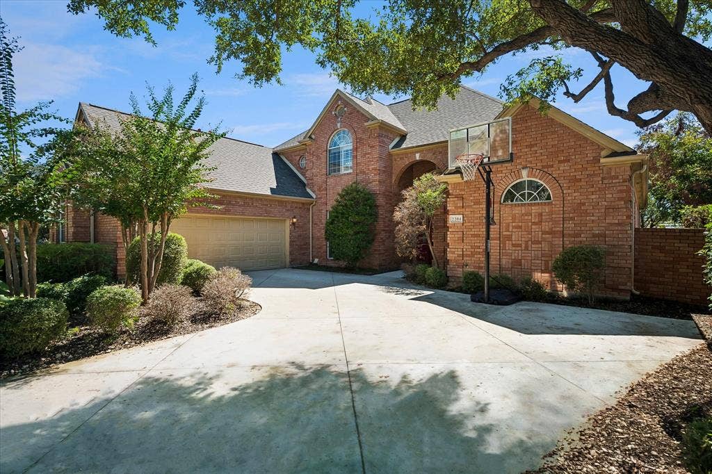 2204 Creekside Circle S, Irving, TX 75063 Brick exterior with arched window details, an attached oversized 2 car garage, and a spacious concrete driveway