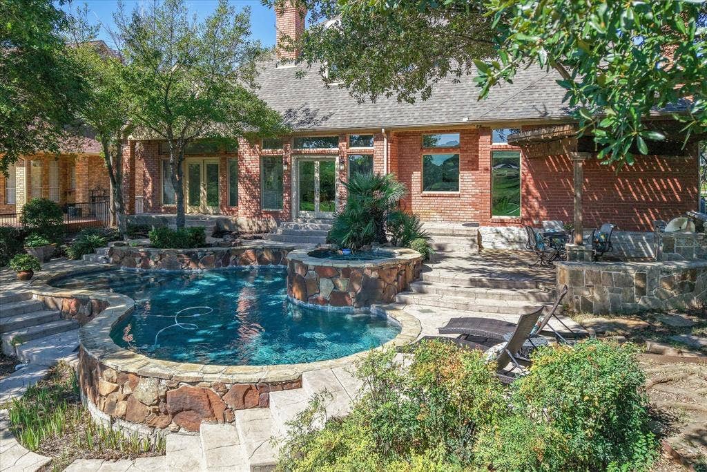 2204 Creekside Circle S, Irving, TX 75063 Brick exterior with multiple French doors, a multi-level pool with stone detailing, spa, and a stone-clad outdoor kitchen area