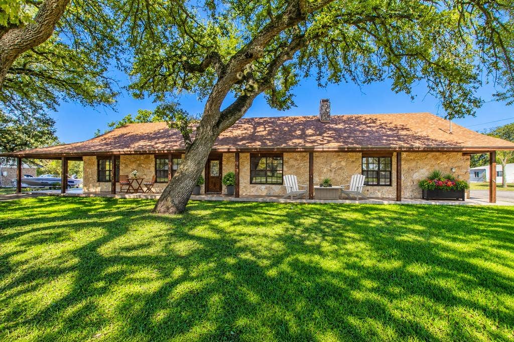 118 Spring Lake Drive, Lacy Lakeview, TX 76705 Stone exterior with a covered front porch and prominent mature trees. Driveway to the covered carport on the left and driveway to the 2 car side garage on the right side! All pictures are virtually staged and the grass is greener in pics!!
