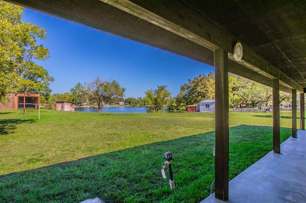118 Spring Lake Drive, Lacy Lakeview, TX 76705 Covered concrete porch, overlooking a grassy expanse, mature trees, and the shoreline of a small lake. Property line goes into the lake. Confirm with a survey. Rumors have it that there are some fish in there!