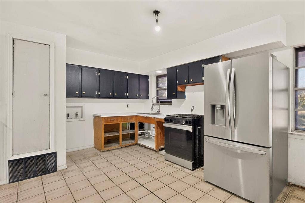 Stainless steel refrigerator and gas range with tile flooring, dark cabinetry, and a single basin sink