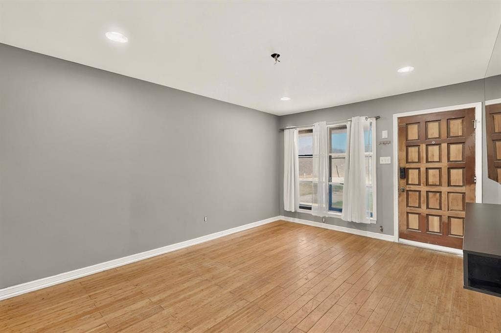 Wood-finish flooring, recessed ceiling lighting, textured entry door, and multiple windows