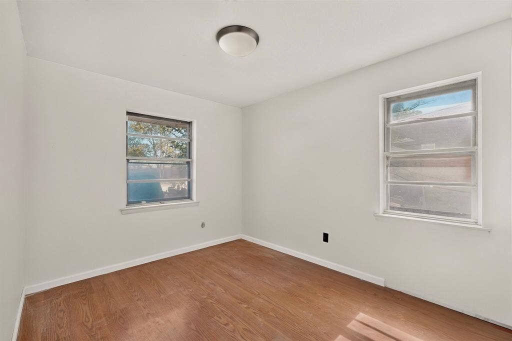 Wood-finish flooring, white painted walls, two windows, and a flush-mount ceiling light