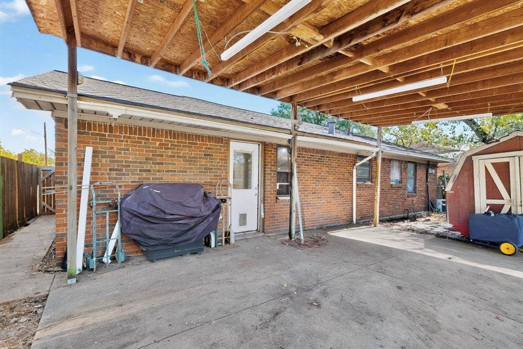 Covered patio area featuring a concrete surface, brick exterior wall, and a wood-framed overhead structure with exposed beams