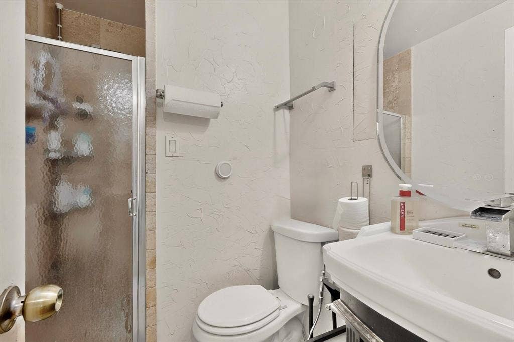 Walk-in shower with frosted glass enclosure, ceramic tile surround, pedestal sink, and wall-mounted mirror