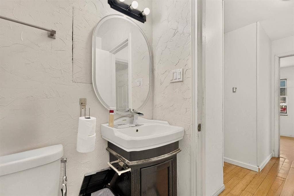 Bathroom featuring an oval mirror, wall-mounted light fixture, pedestal sink, and wood-finish flooring